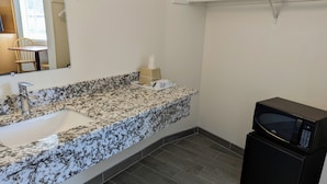 A bathroom with a granite countertop sink, a mirror, a towel dispenser, and a black microwave. - Royal Inn (South San Francisco)