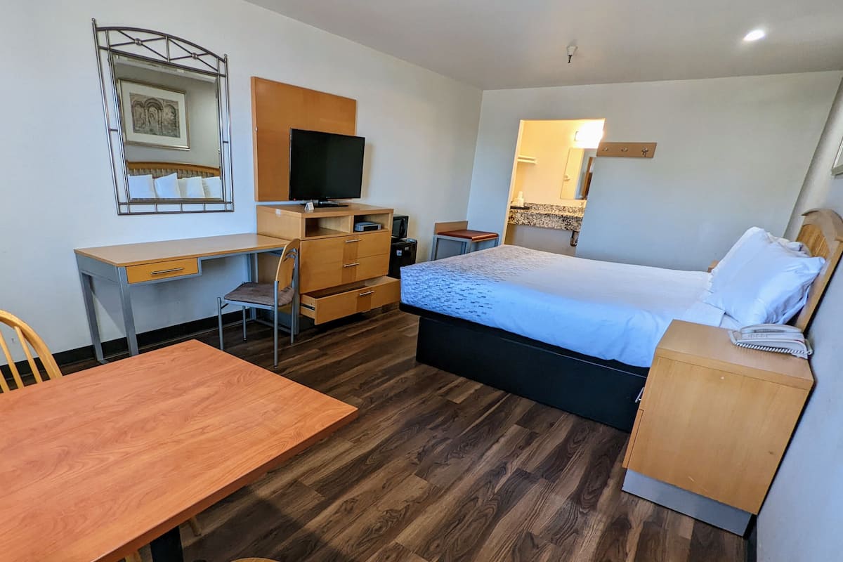 Une chambre d’hôtel avec un bureau en bois, un lit recouvert d’une couverture bleue, une télévision, un miroir et une petite table.