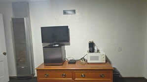 A room with a television on a wooden dresser, a microwave, and a coffee maker.