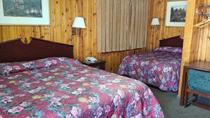A room with two beds, wooden walls, a small table, and two wall-mounted lamps.