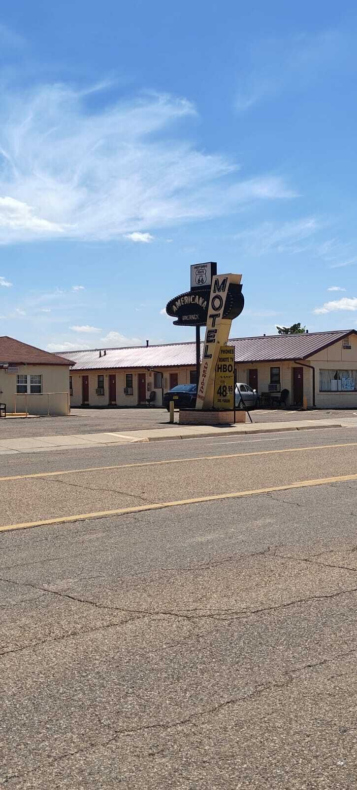 A motel with a large sign, a parking lot, and buildings in the background.
