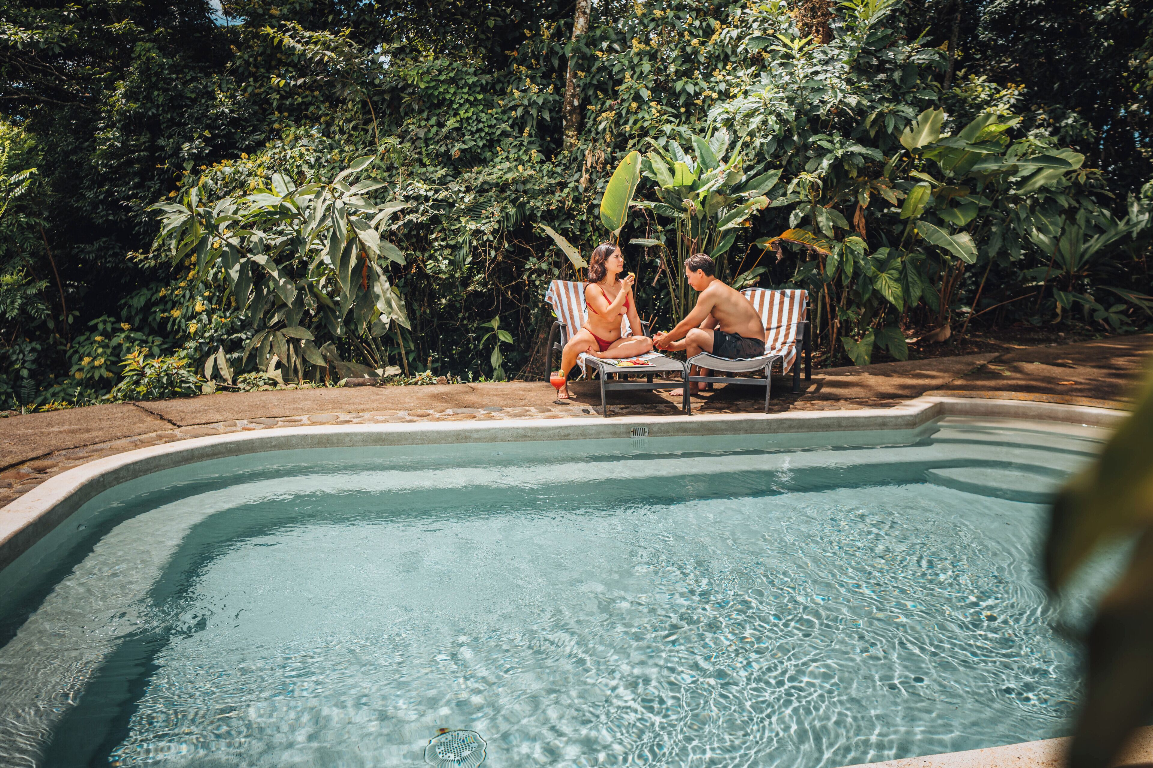 A swimming pool with two lounge chairs and a person in the water.