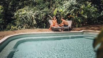 A swimming pool with two lounge chairs and a person in the water.