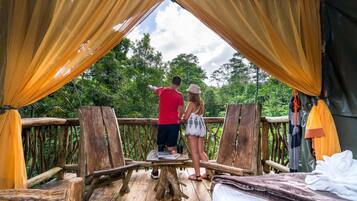 A wooden deck with a table and chairs, overlooking a forested area.
