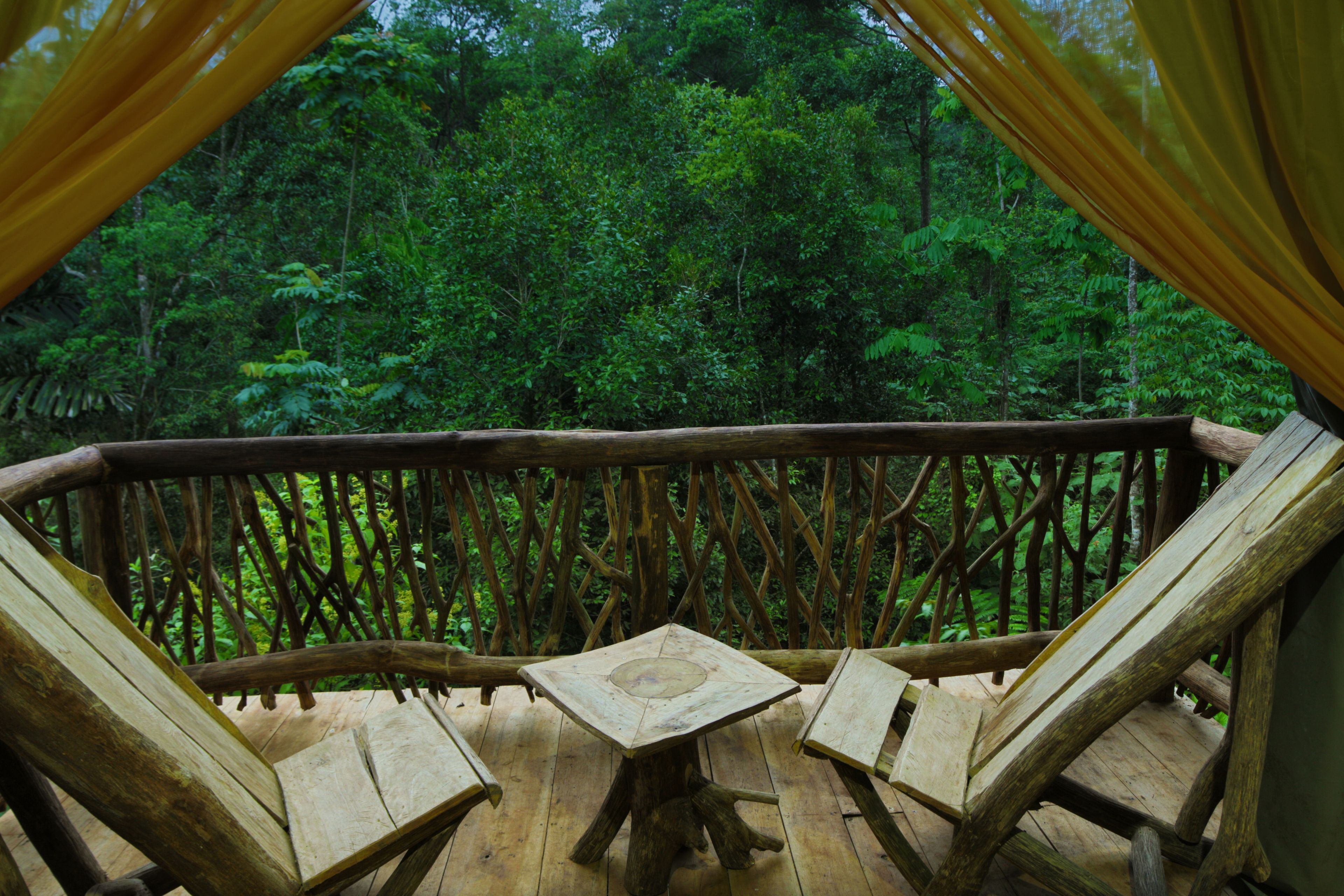 Una terraza de madera con una mesa y sillas, rodeada por barandilla de madera, con vistas a un bosque frondoso.