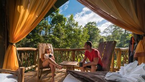 A wooden deck with a bed, a table, and two people sitting. - La Tigra Rainforest Lodge (San Lorenzo)