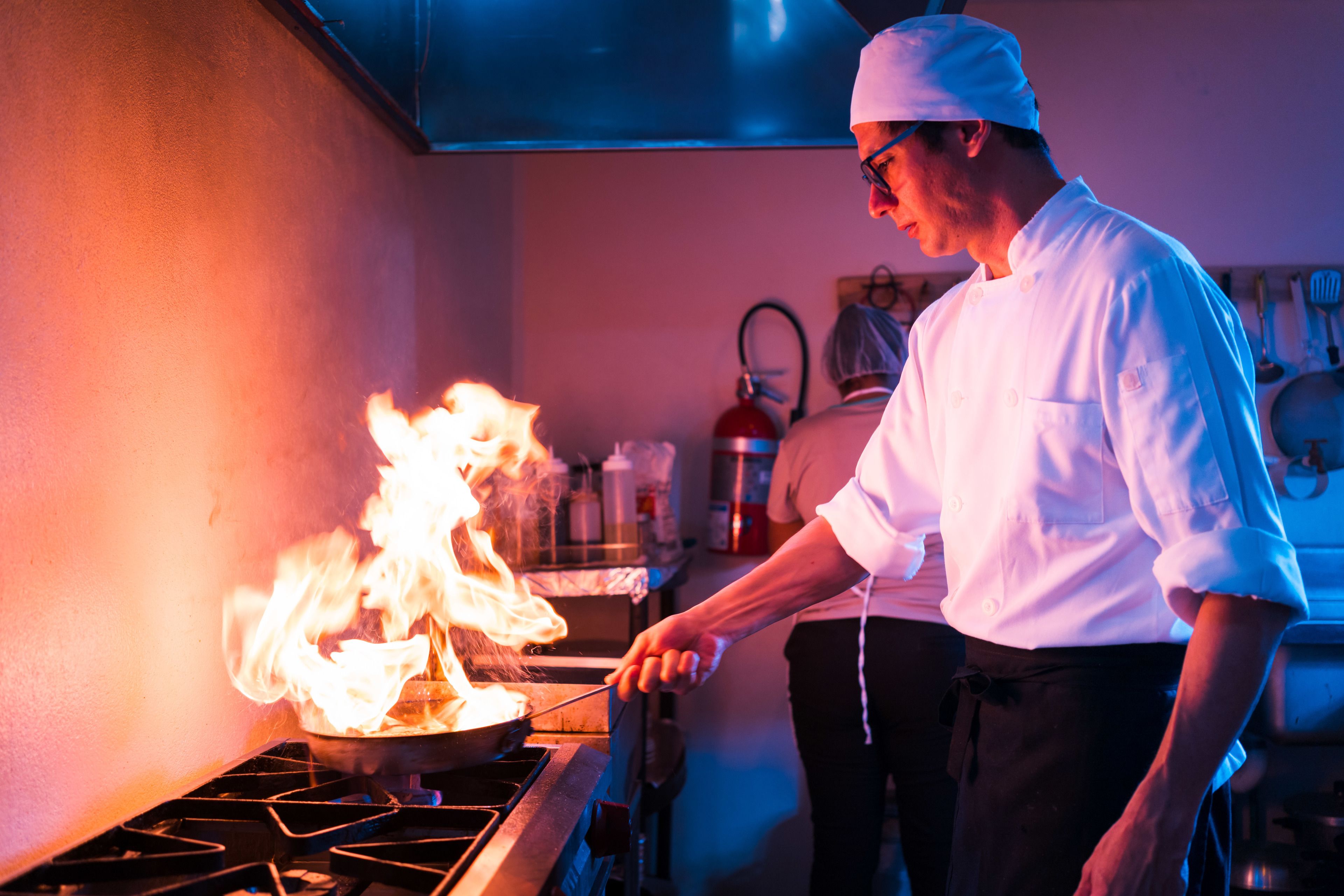 A chef cooking with flames on a stove in a kitchen.