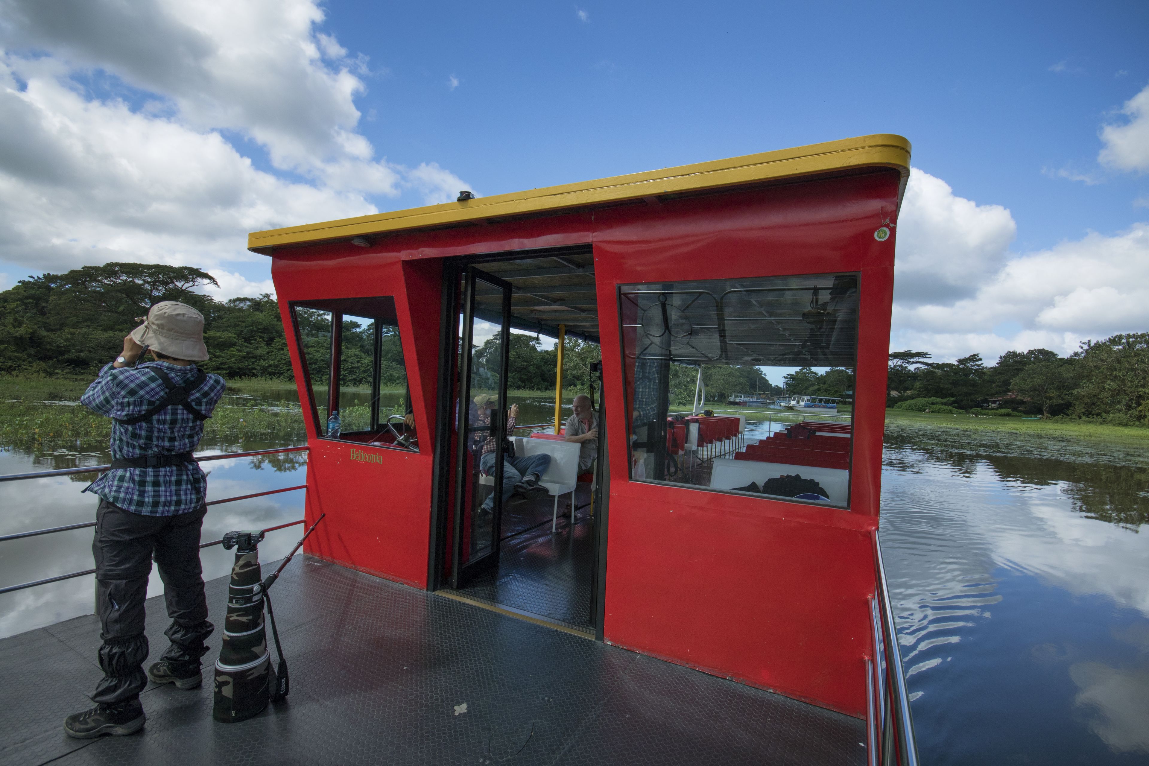 A red boat with a yellow roof, a person standing on the deck, and another person inside.