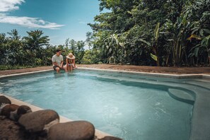 Une piscine où se trouvent deux personnes, entourée d’une végétation luxuriante.