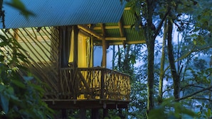 A treehouse with a wooden deck and a metal roof, surrounded by dense foliage. - La Tigra Rainforest Lodge (San Lorenzo)