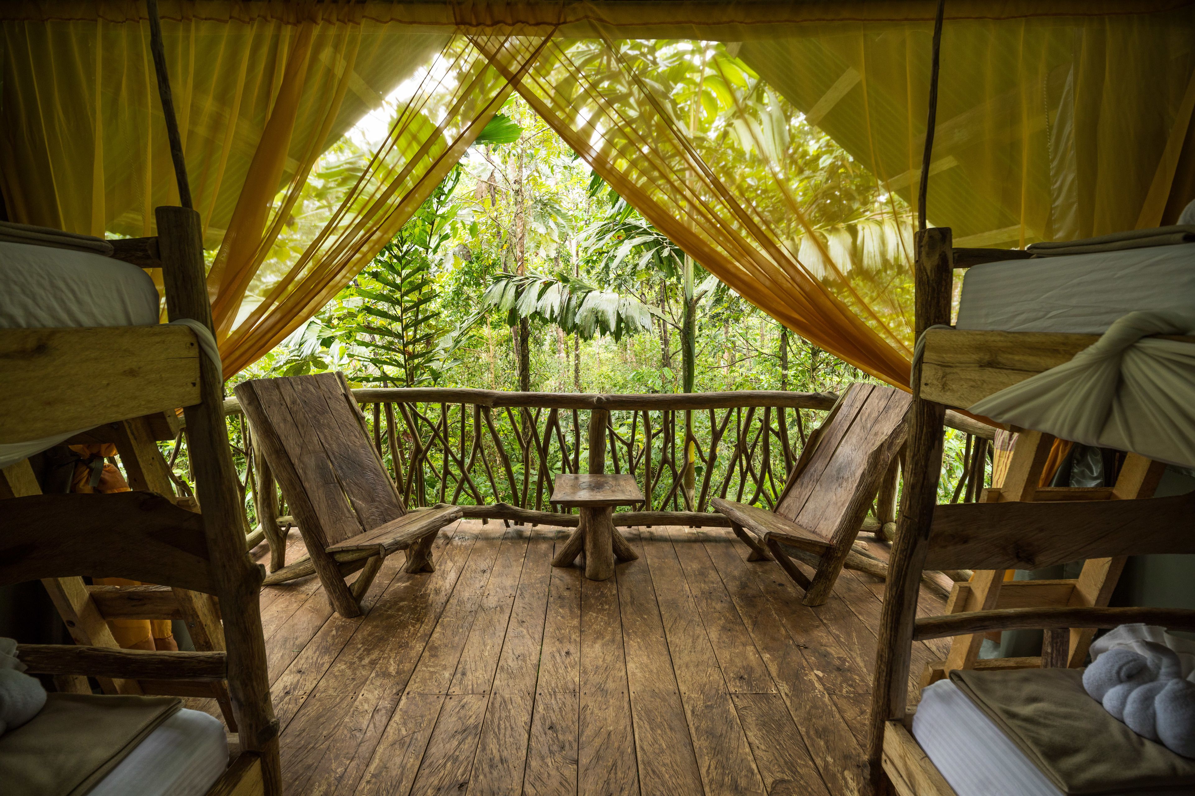 Une terrasse en bois avec deux chaises et une table en bois, entourée d’une clôture en bois et recouverte d’un tissu jaune.