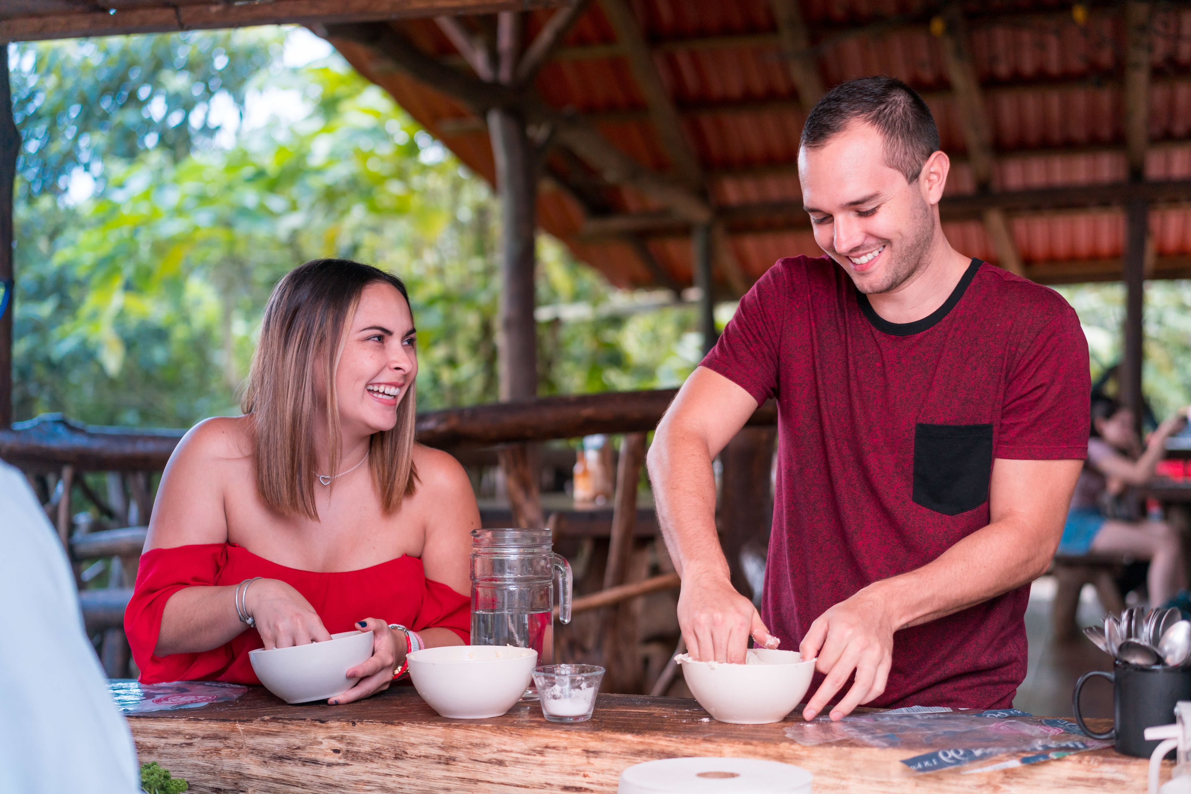 Una pareja preparando comida en una mesa de madera al aire libre, en un entorno rústico.