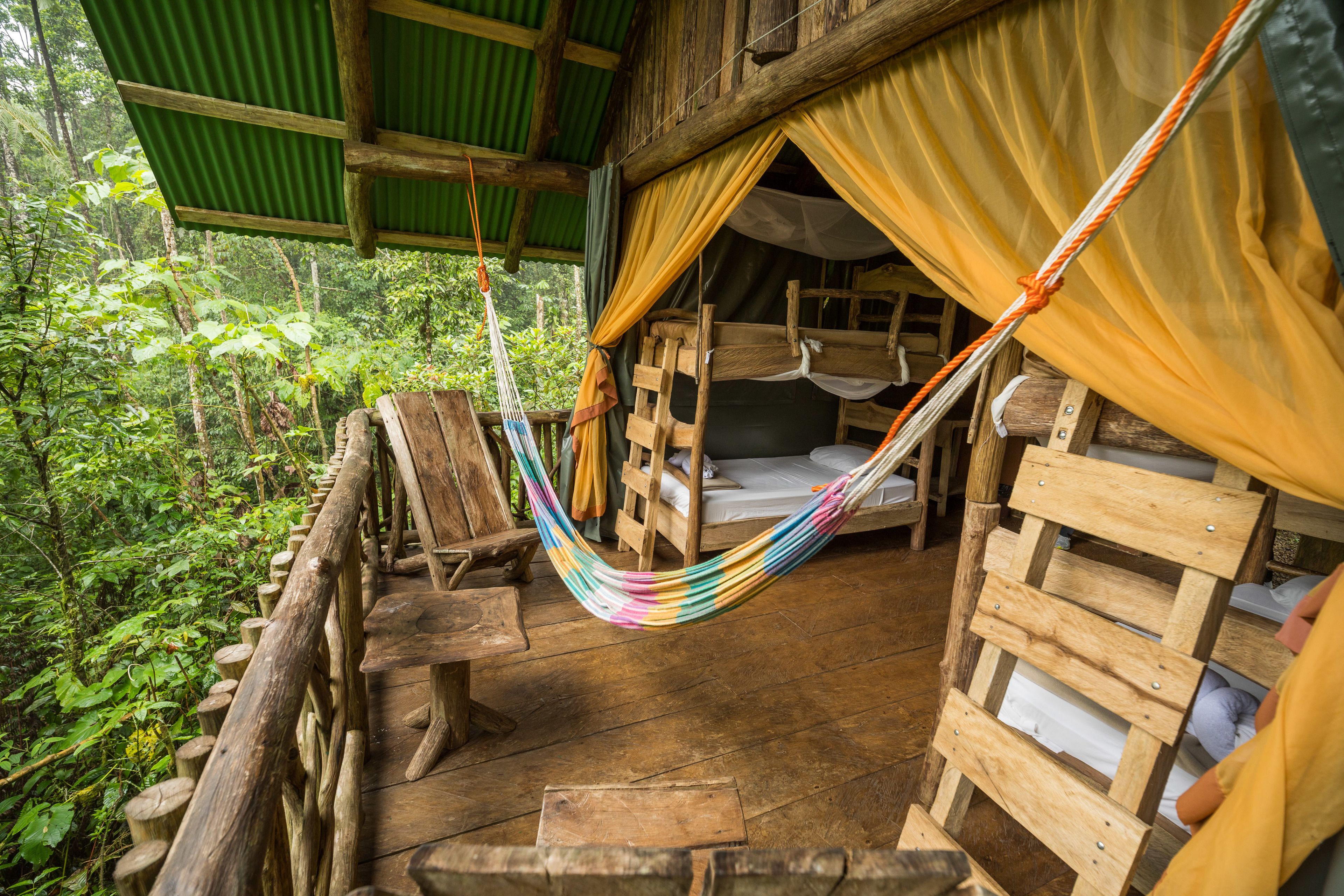 Une cabane en bois rustique, dotée d’un hamac, d’une terrasse en bois et d’un lit avec un matelas et des oreillers.