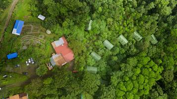 An aerial view of a rural area with several buildings, including a large house with a red roof, surrounded by dense green forest.