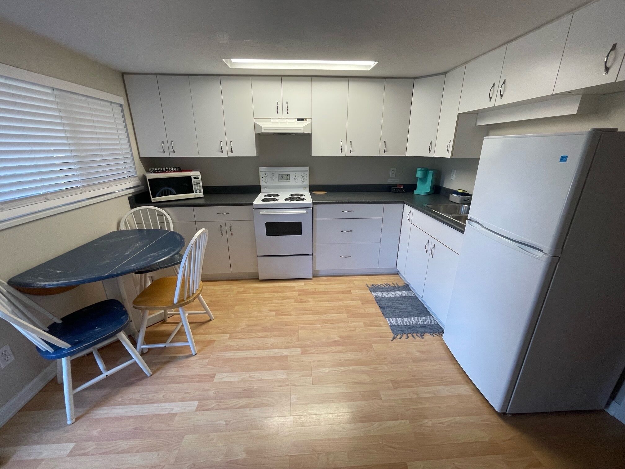 A compact kitchen with white cabinets, a microwave, stove, and a refrigerator. There is a small dining table with two chairs.