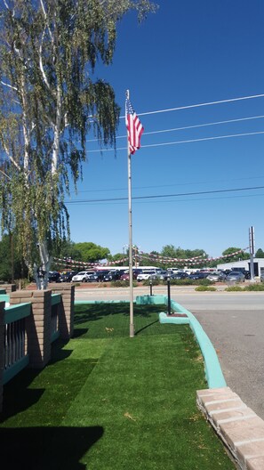 A flagpole with an American flag, a parking lot, and a grassy area with a brick border. - Cortez Cozy Inn (Cortez)