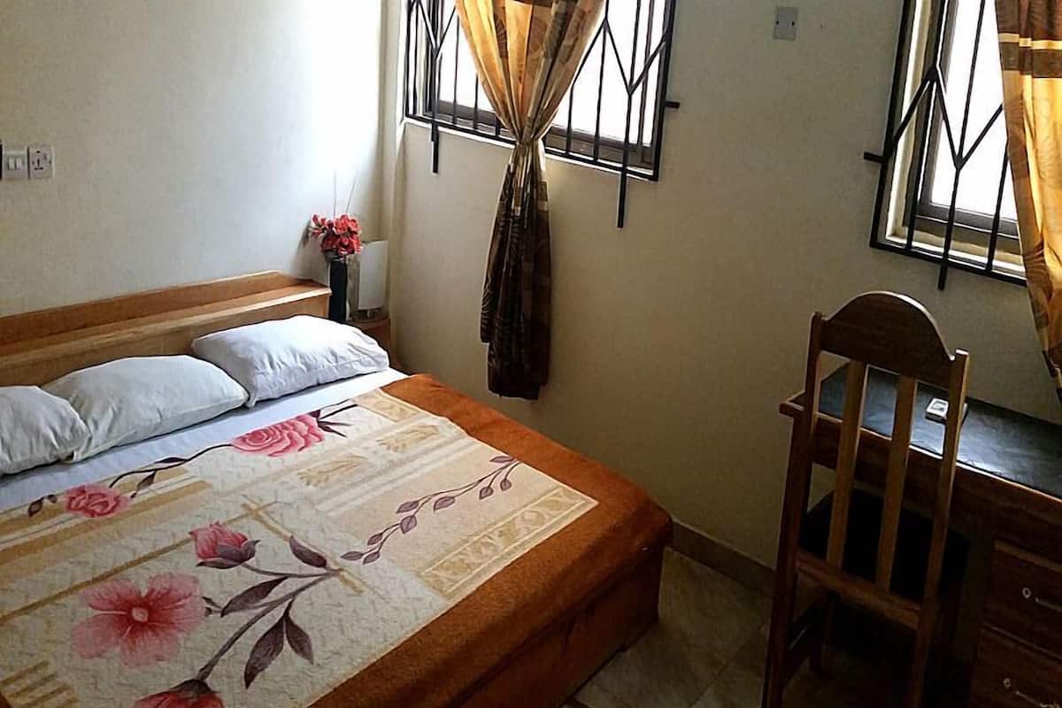 A bedroom with a bed, a chair, a desk, and a window with curtains.
