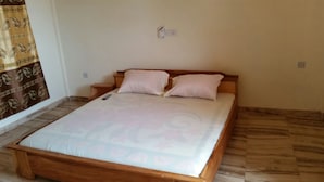 Una habitación con una cama de madera, dos almohadas, una mesita de noche y una cortina.
