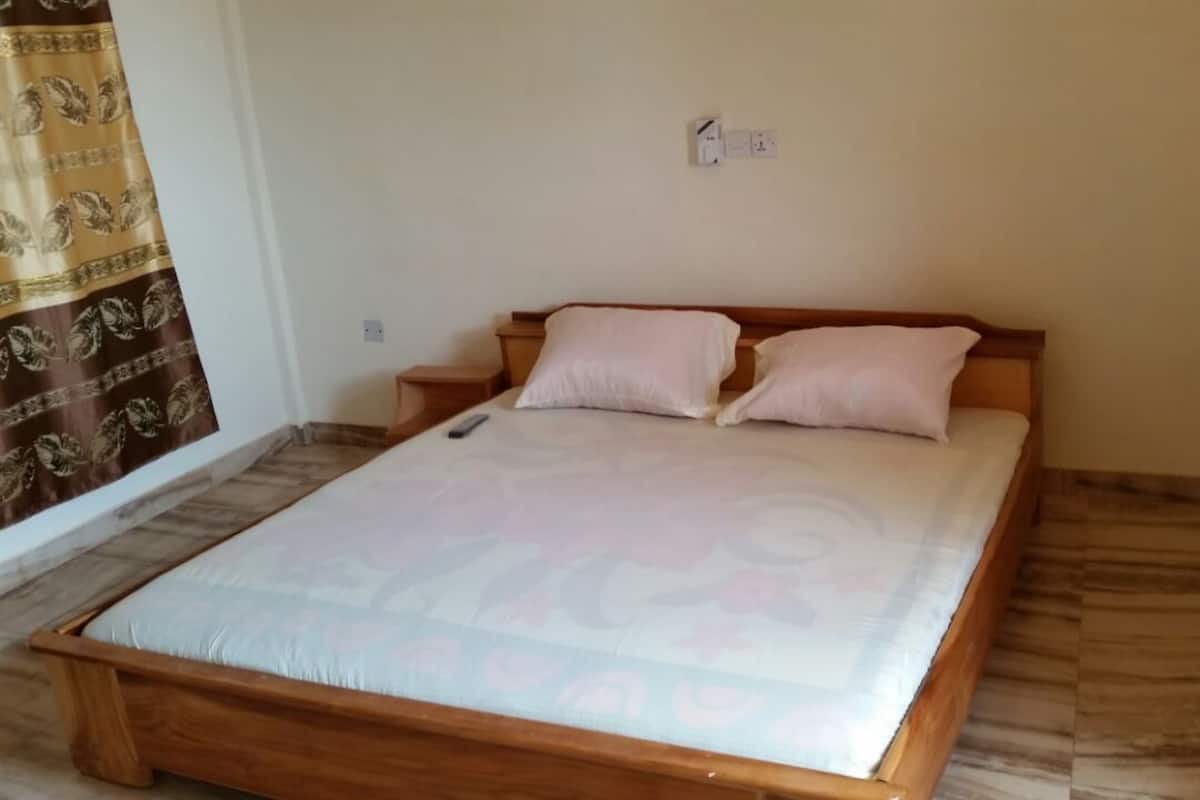 A room with a wooden bed, two pillows, a nightstand, and a curtain.
