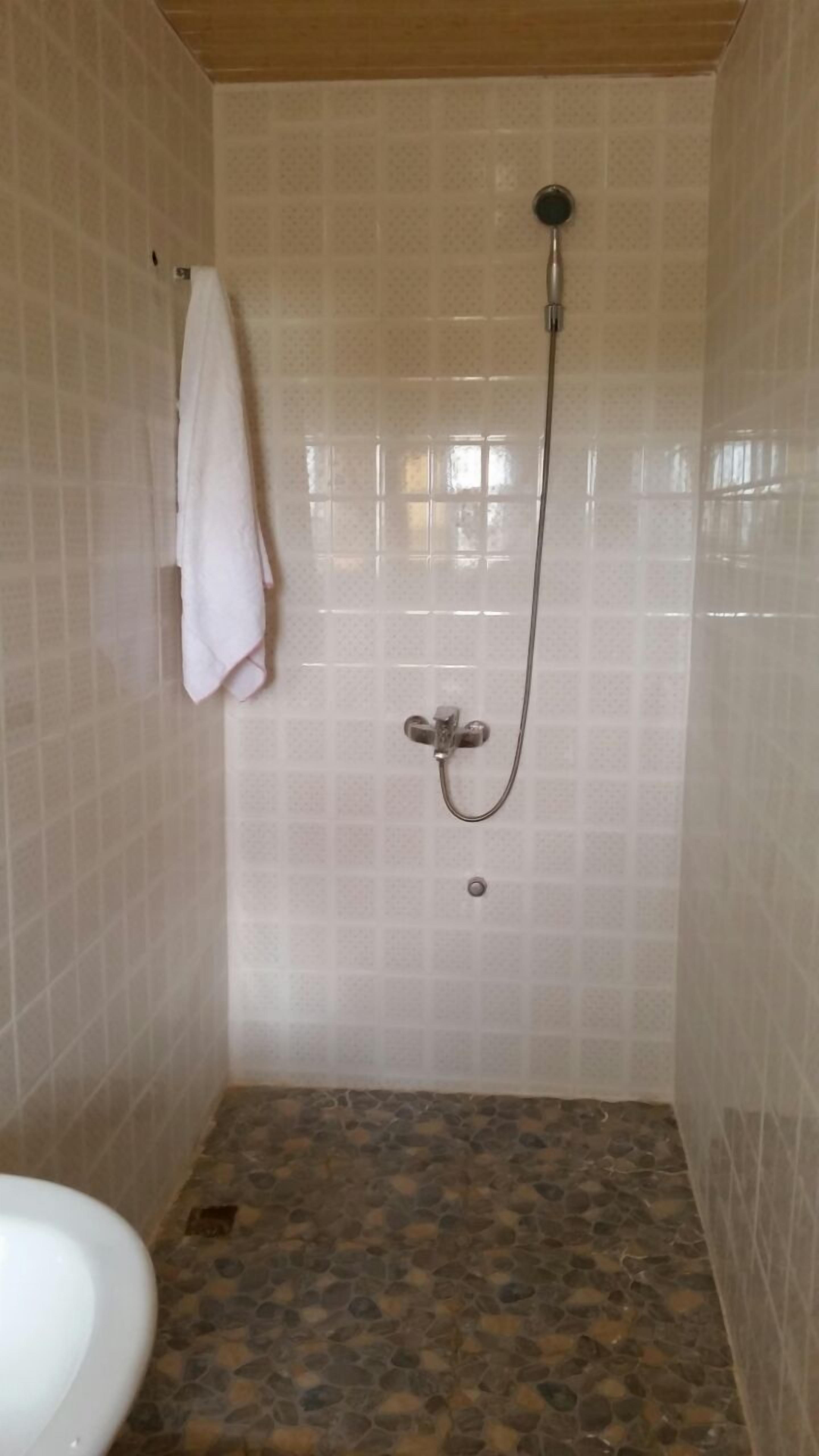 A small, tiled bathroom with a shower, a toilet, and a towel hanging on the wall.