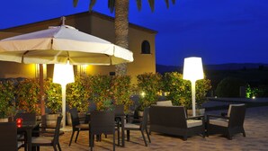 An outdoor patio area with tables and chairs, a palm tree, and a building in the background. - Can Bonastre Wine Resort, The Originals Relais (Relais du Silence) (Masquefa)
