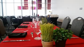 Une salle de conférence avec une table rouge préparée pour une réunion, équipée de chaises, d’un verre et d’une plante en pot.