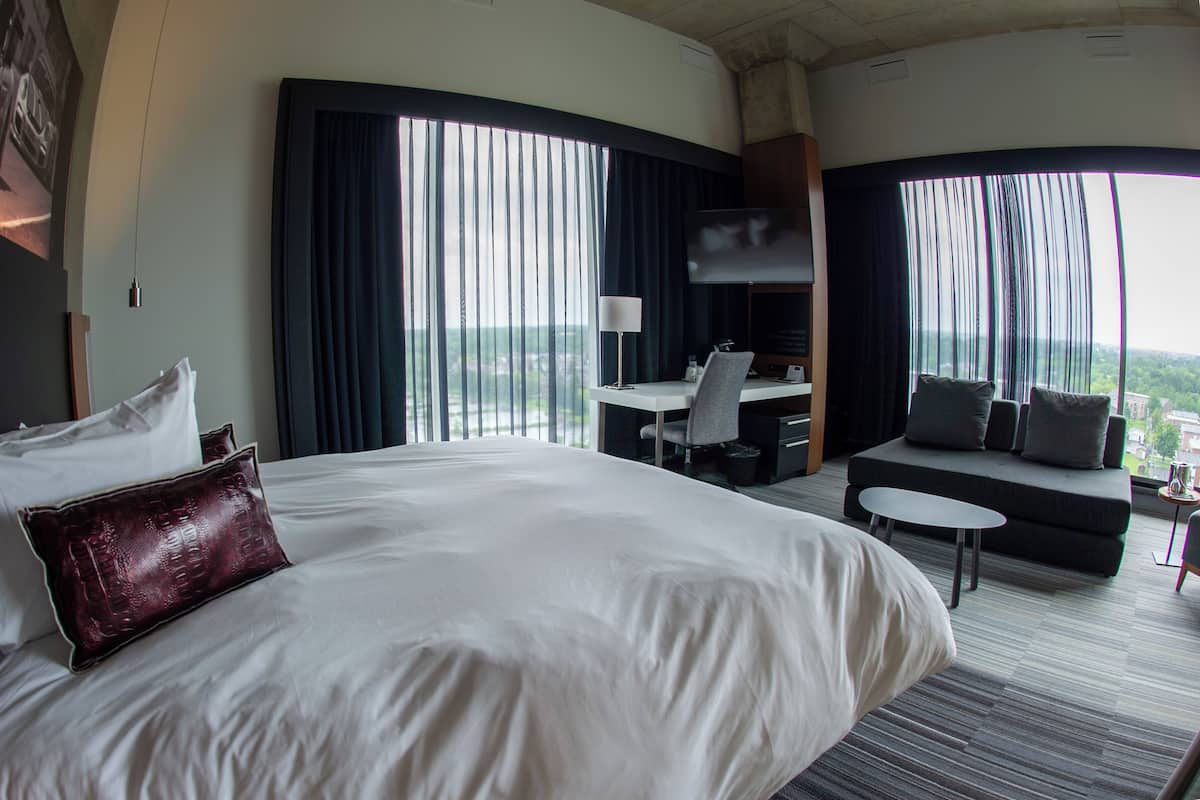 A hotel room with a large bed, a desk, a sofa, and a TV.