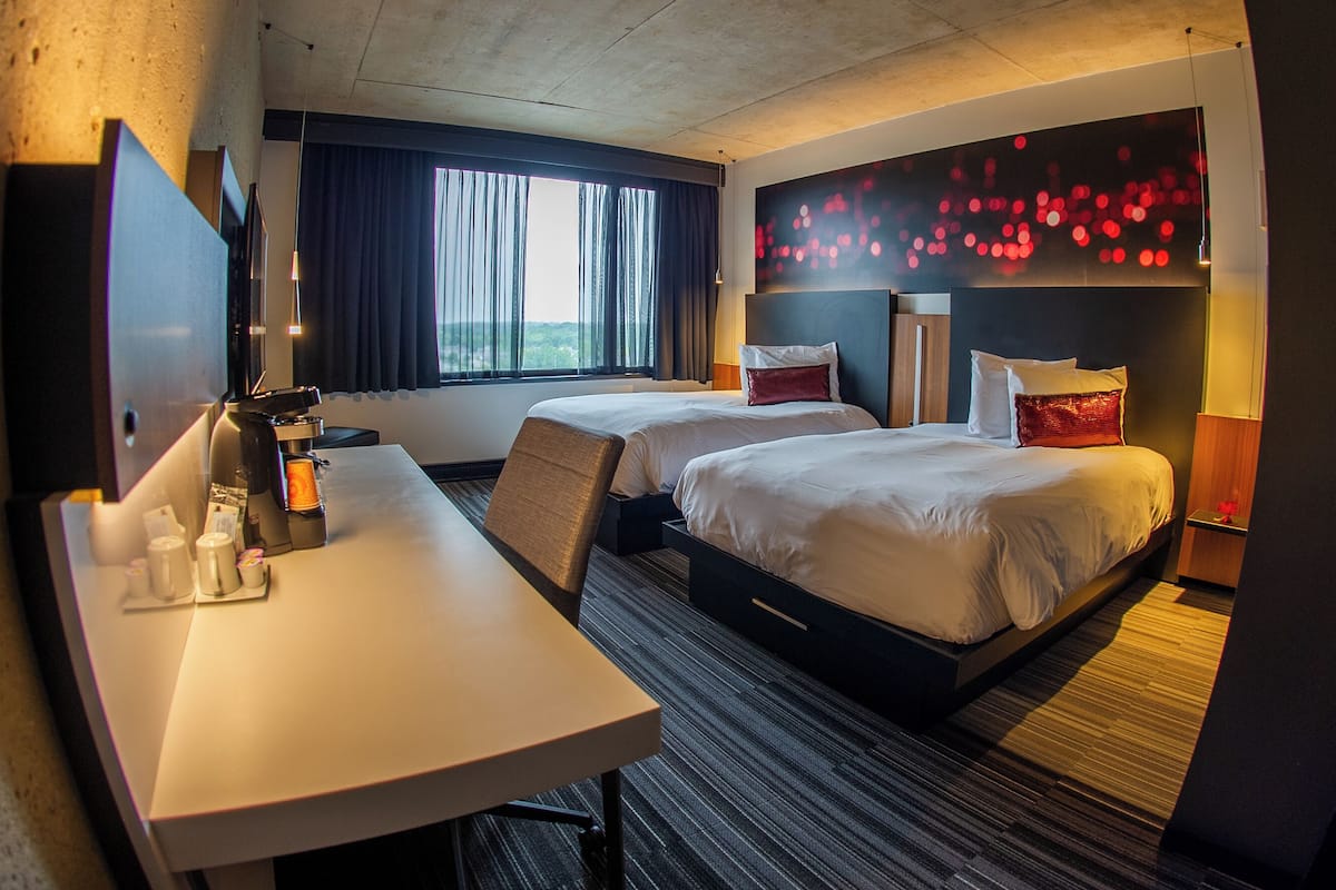 A hotel room with a bed, a desk, a TV, and a window with curtains.