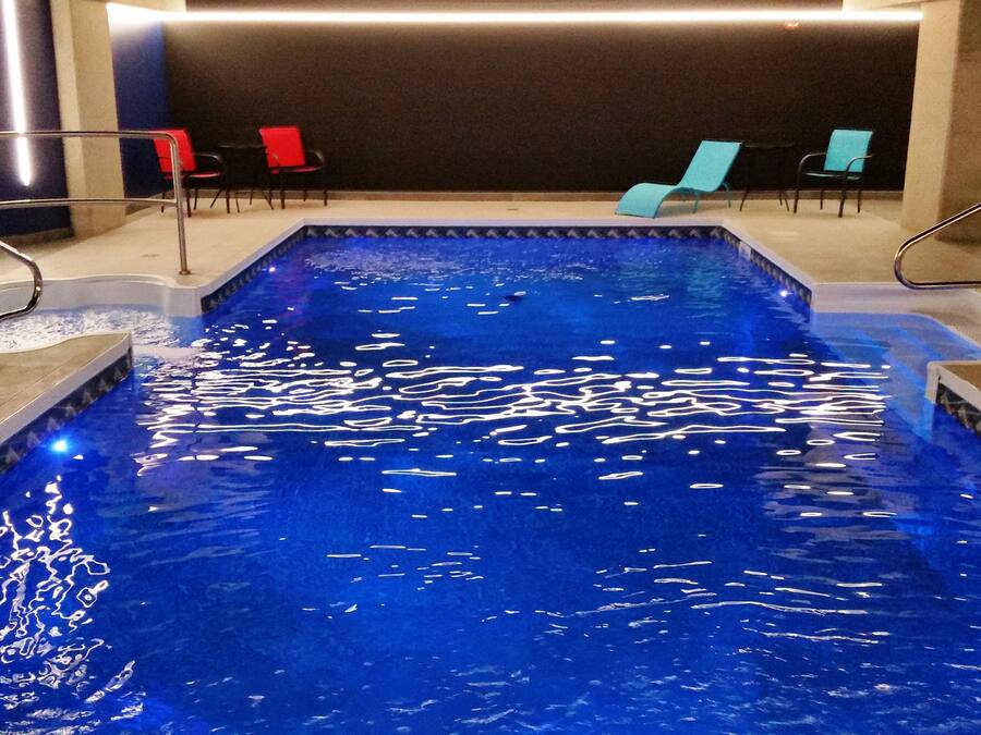 An indoor swimming pool with clear blue water, surrounded by lounge chairs and a modern interior design.