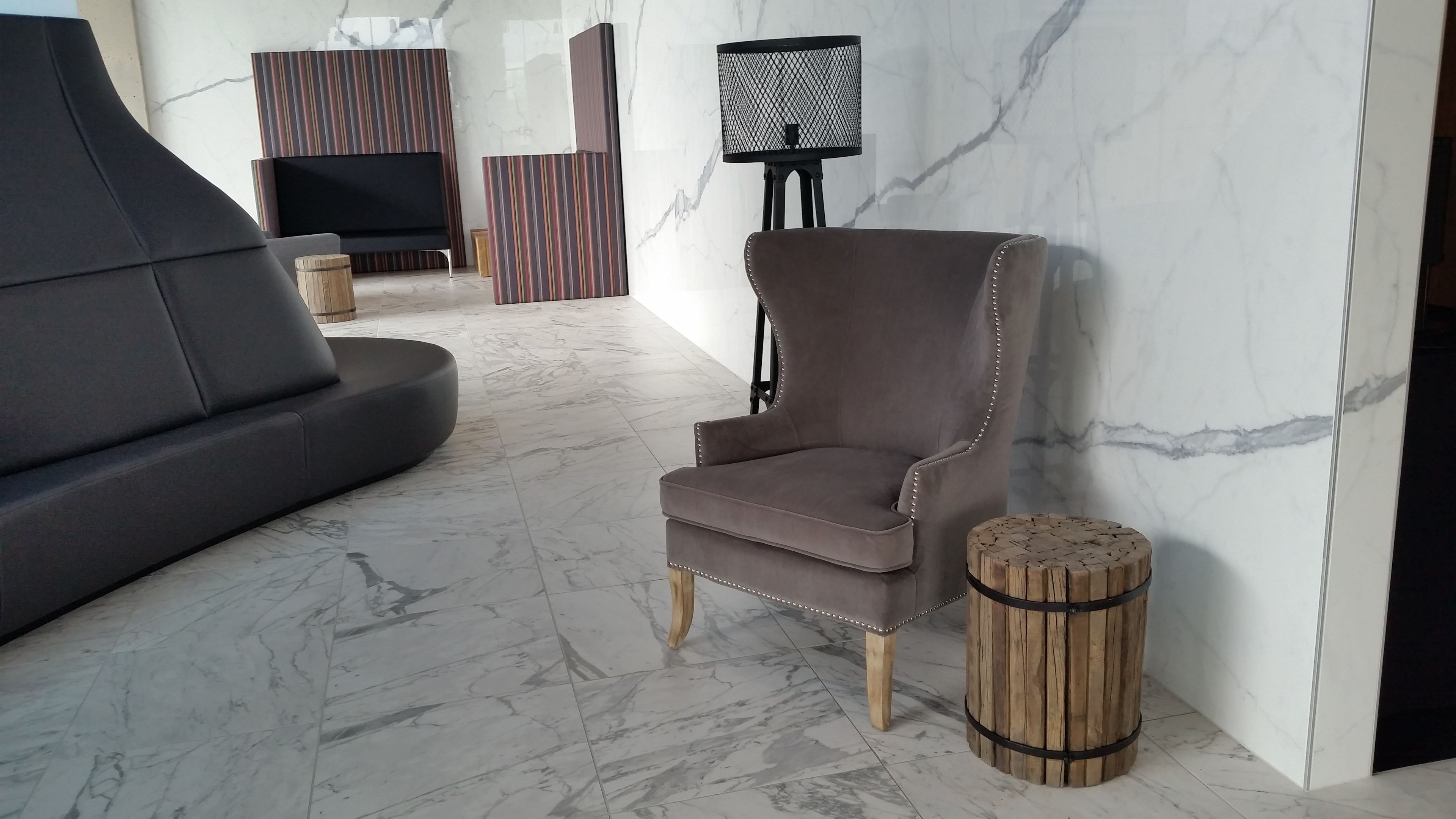 Una sala de estar moderna con un sofá seccional, un sillón marrón, un taburete redondo de madera y un televisor sobre un mueble bajo.