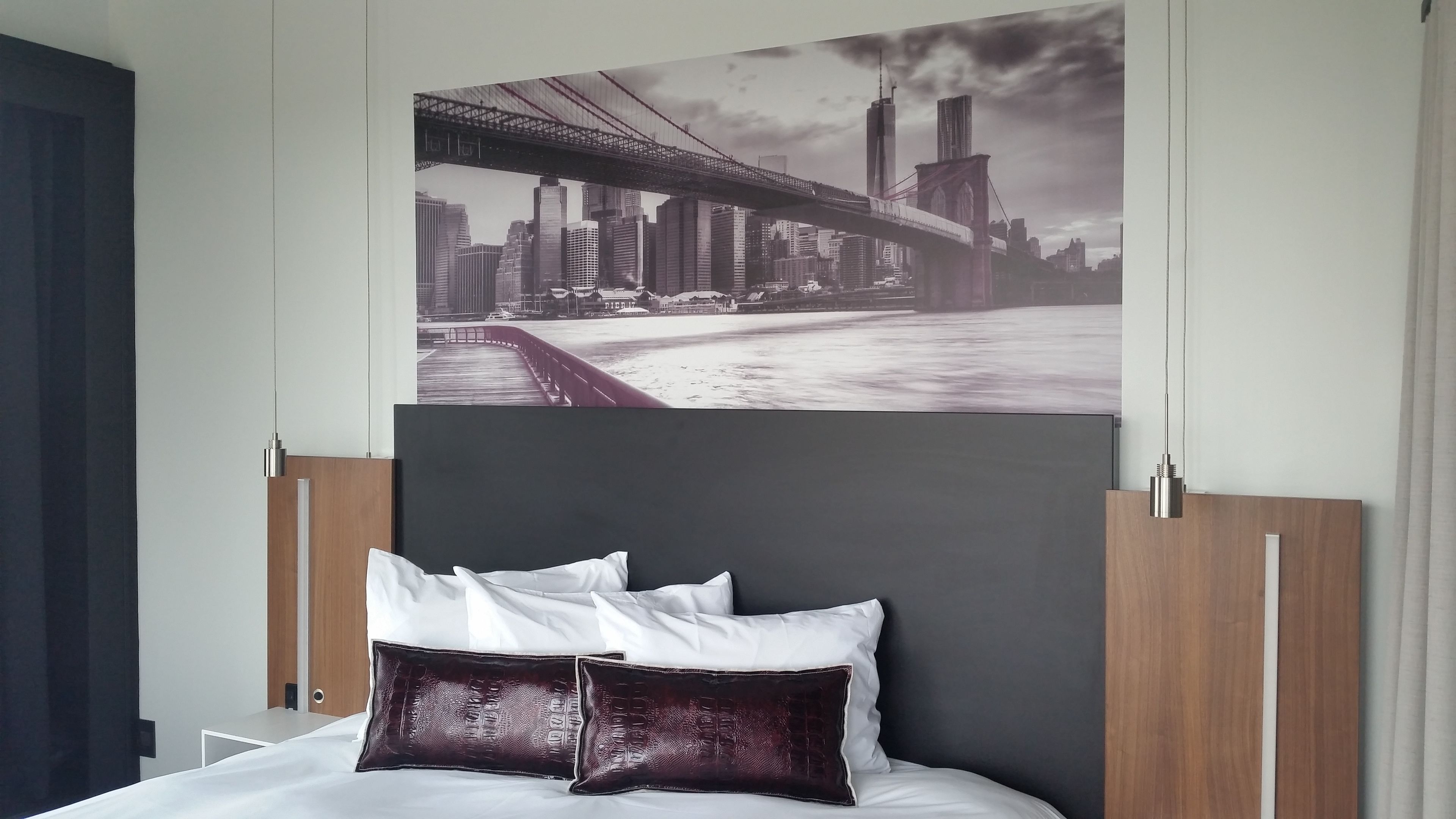 A bedroom with a bed, pillows, a headboard, and a cityscape wall art.