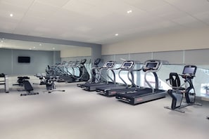 Un gimnasio con varias cintas de correr, máquinas de pesas y un amplio espejo.