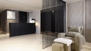 Un área de recepción moderna con un mostrador, un cartel de sala privada y un sillón de masaje.