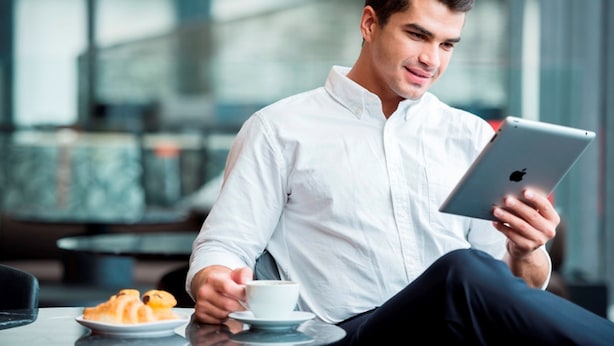 Una persona sentada a una mesa con una tableta y una taza de café, con croissants sobre la mesa.