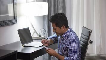 Un homme est assis à un bureau, devant un ordinateur portable, et il écrit.