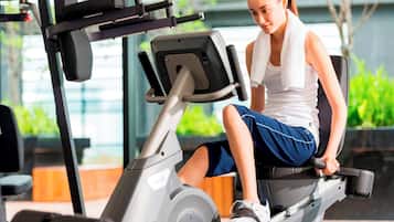 A woman using a stationary bike in a gym with a window view.