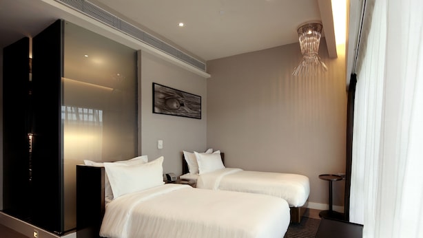 Une chambre d’hôtel moderne avec deux lits, une grande fenêtre avec des rideaux, une œuvre d’art accrochée au mur et un luminaire au plafond.