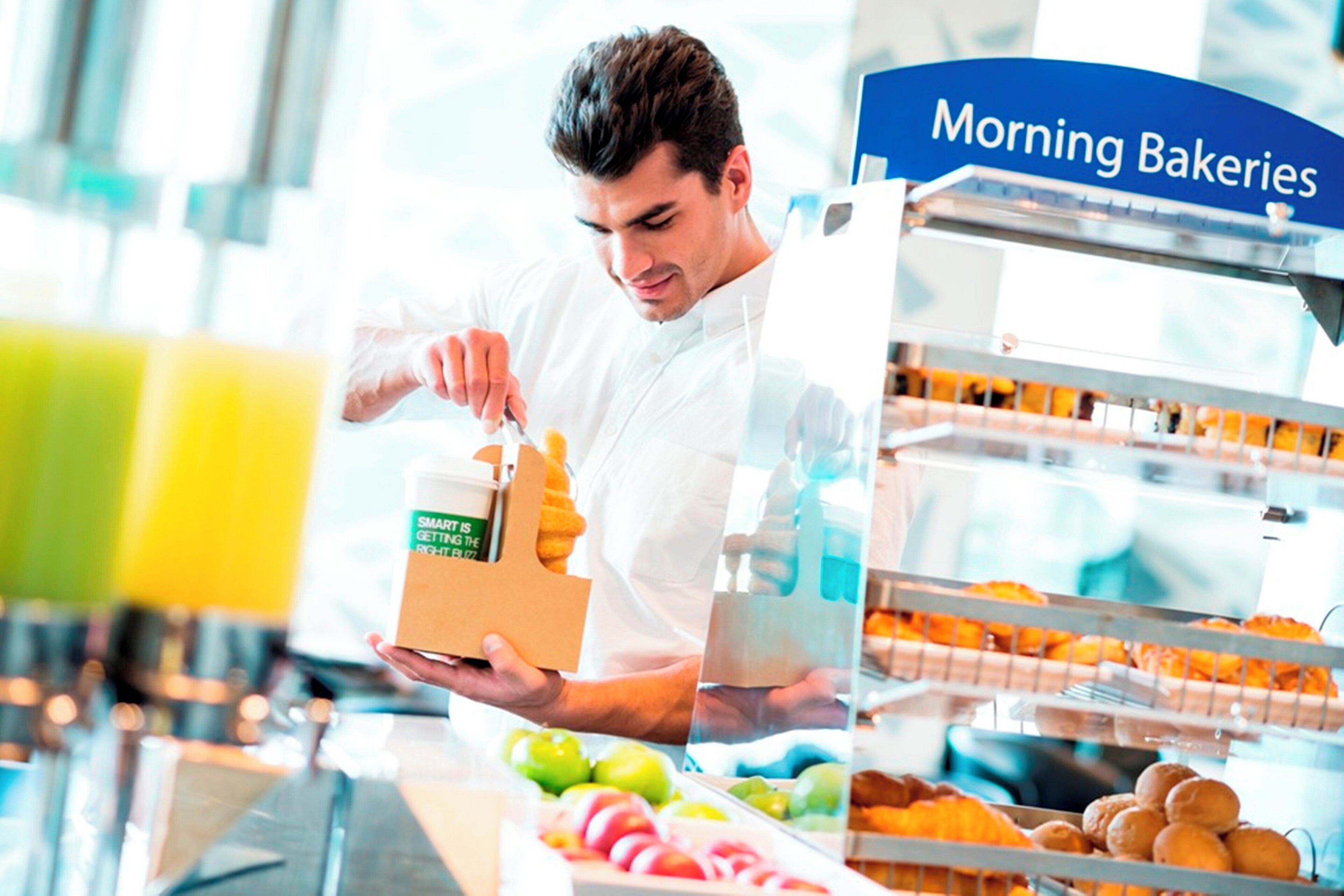 Una persona con camisa blanca manipula una caja con la etiqueta que dice 'SMART IS GETTING THE RHIT BLZZ' en una sección de panadería identificada como 'Morning Bakeries'.