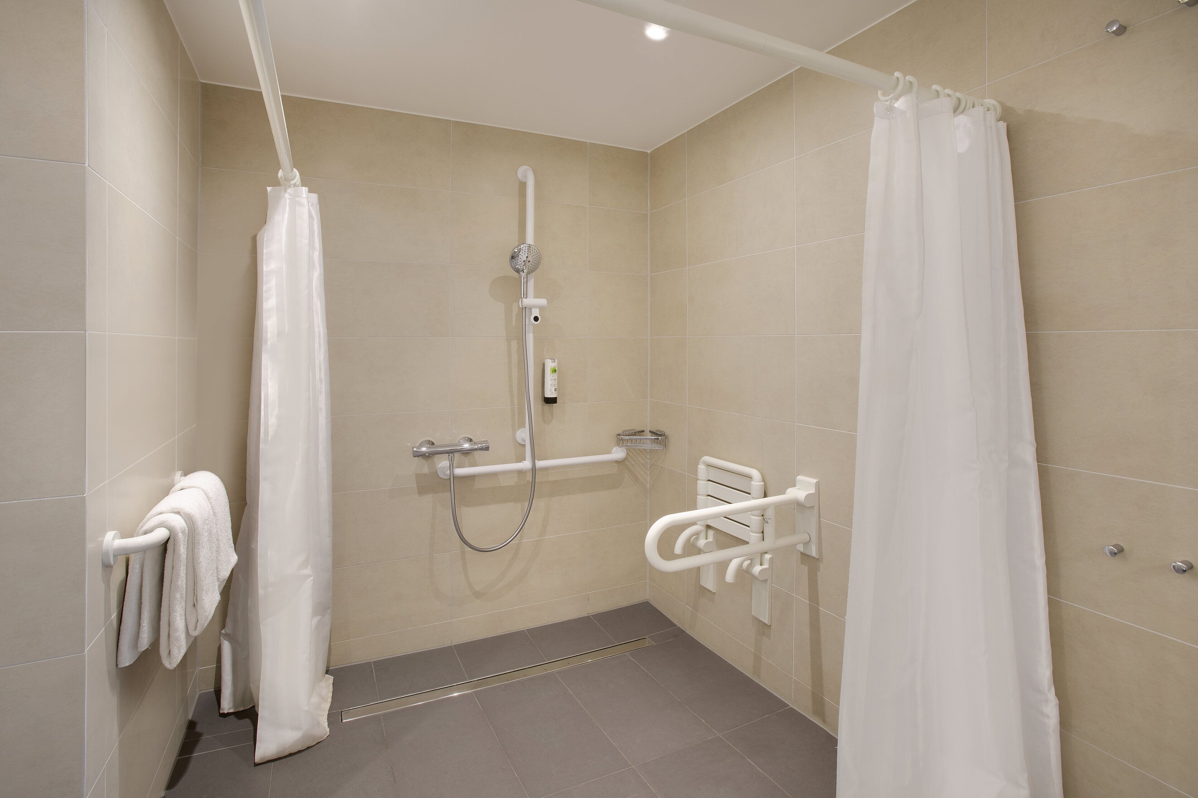 Un baño moderno con ducha, barras de apoyo y un perchero para toallas.