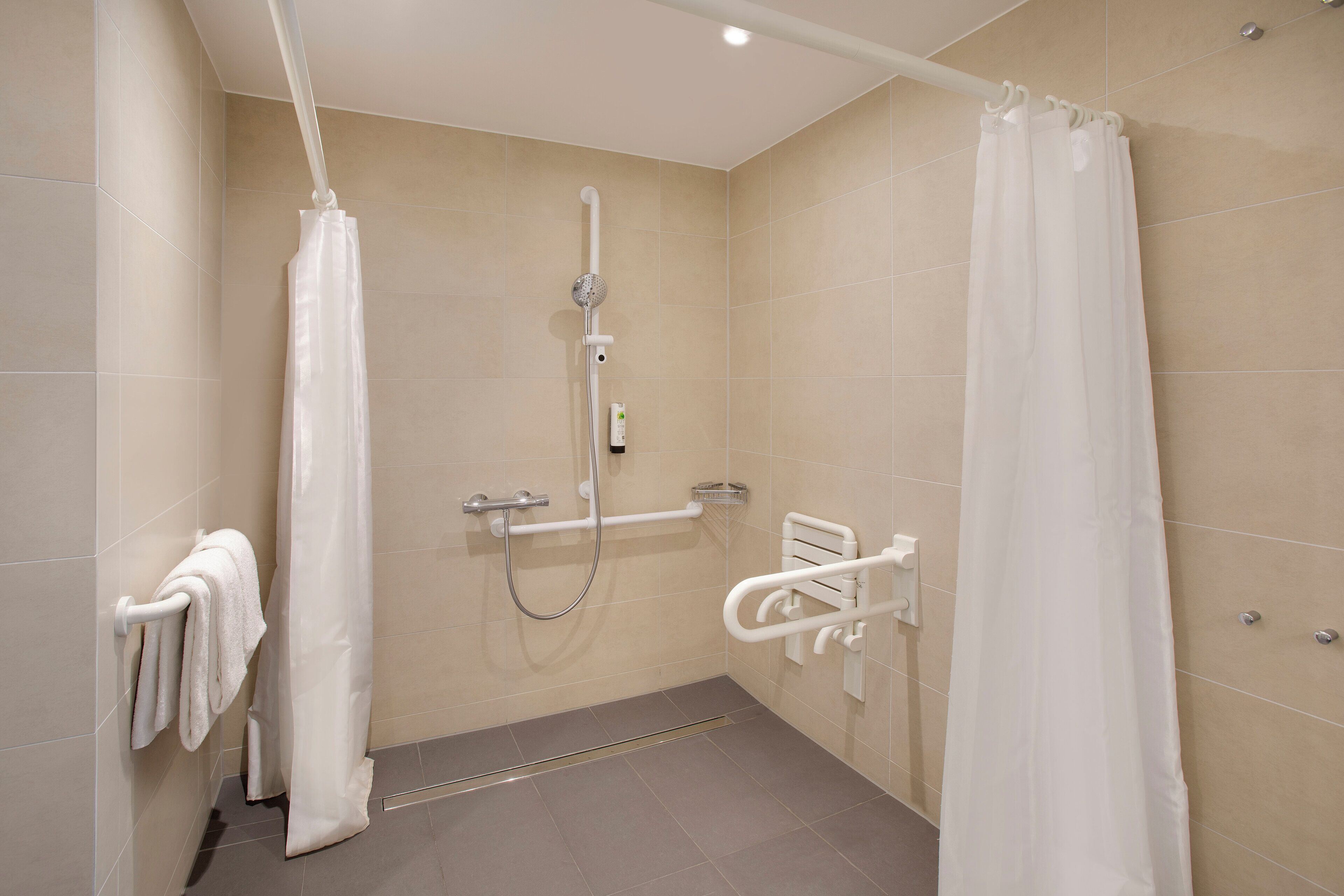 Un baño moderno con ducha, barras de apoyo y un perchero para toallas.