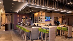 A modern bar area with a long counter, green bar stools, and a television screen.