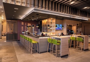 A modern bar area with a long counter, green bar stools, and a television screen.