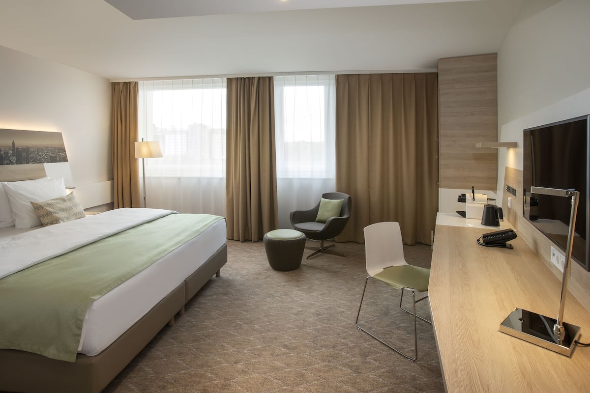 A hotel room with a bed, a desk, a chair, a TV, and a window with curtains.