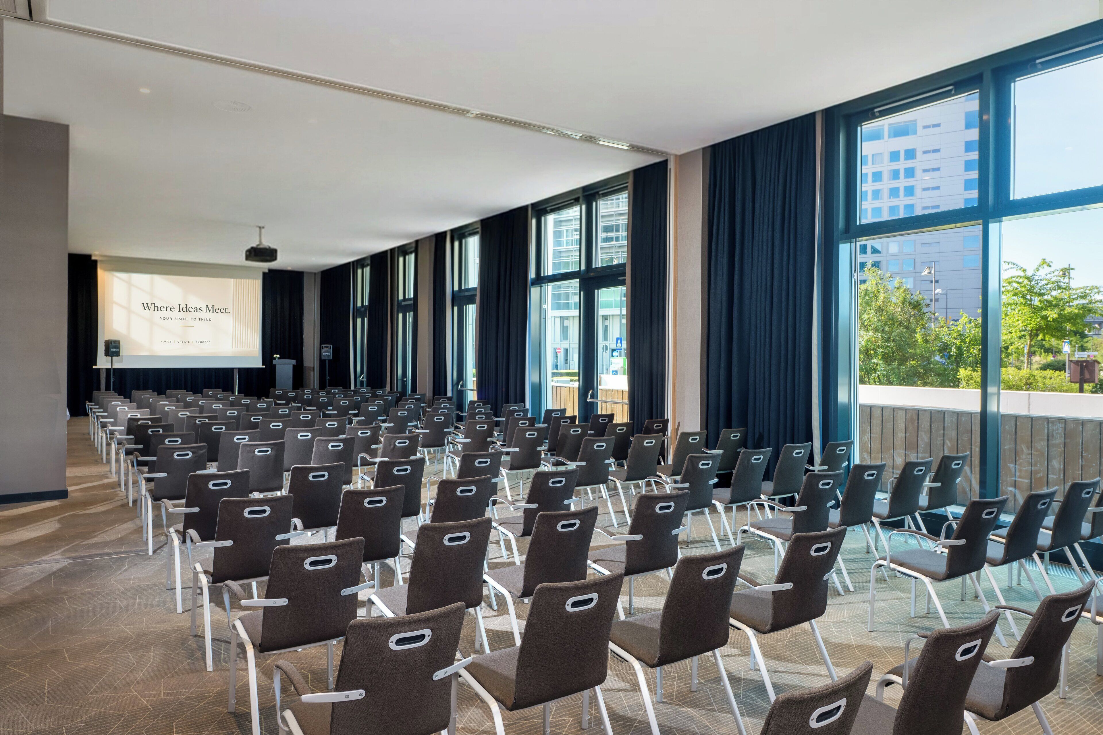 A conference room with rows of chairs, large windows, and a presentation screen.