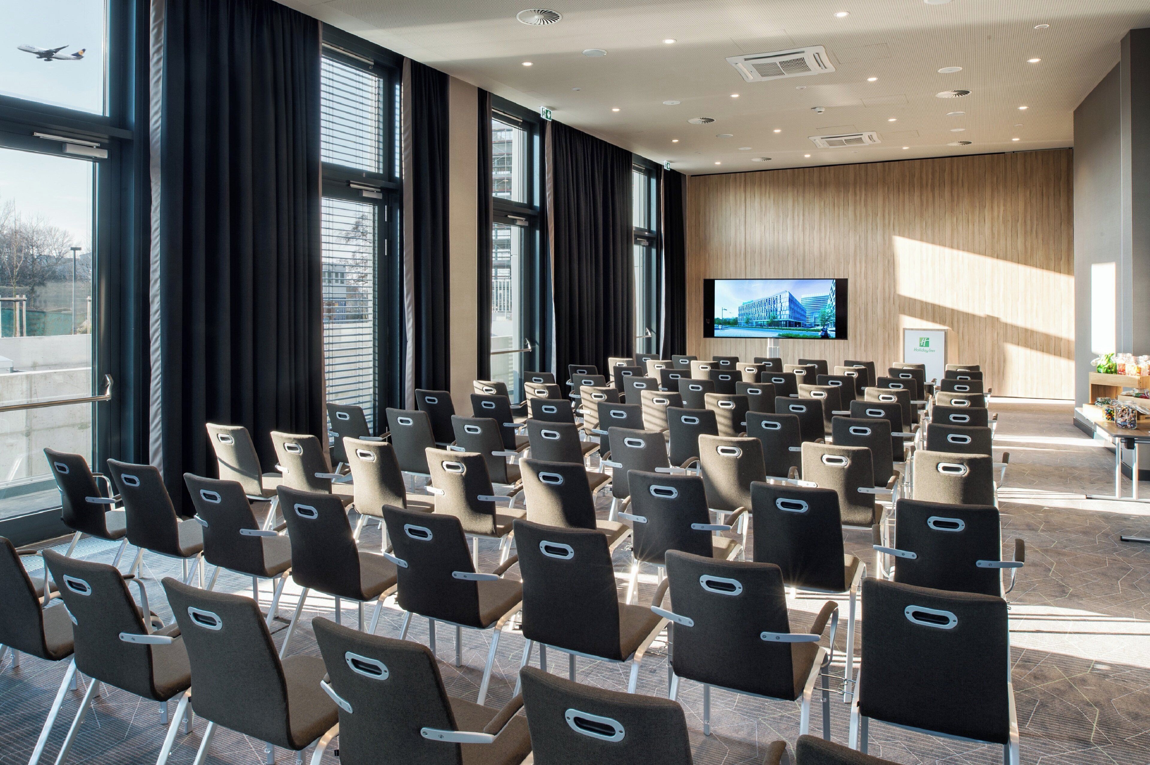 Una sala conferenze con file di sedie, un grande schermo e il cartello di Holiday Inn.