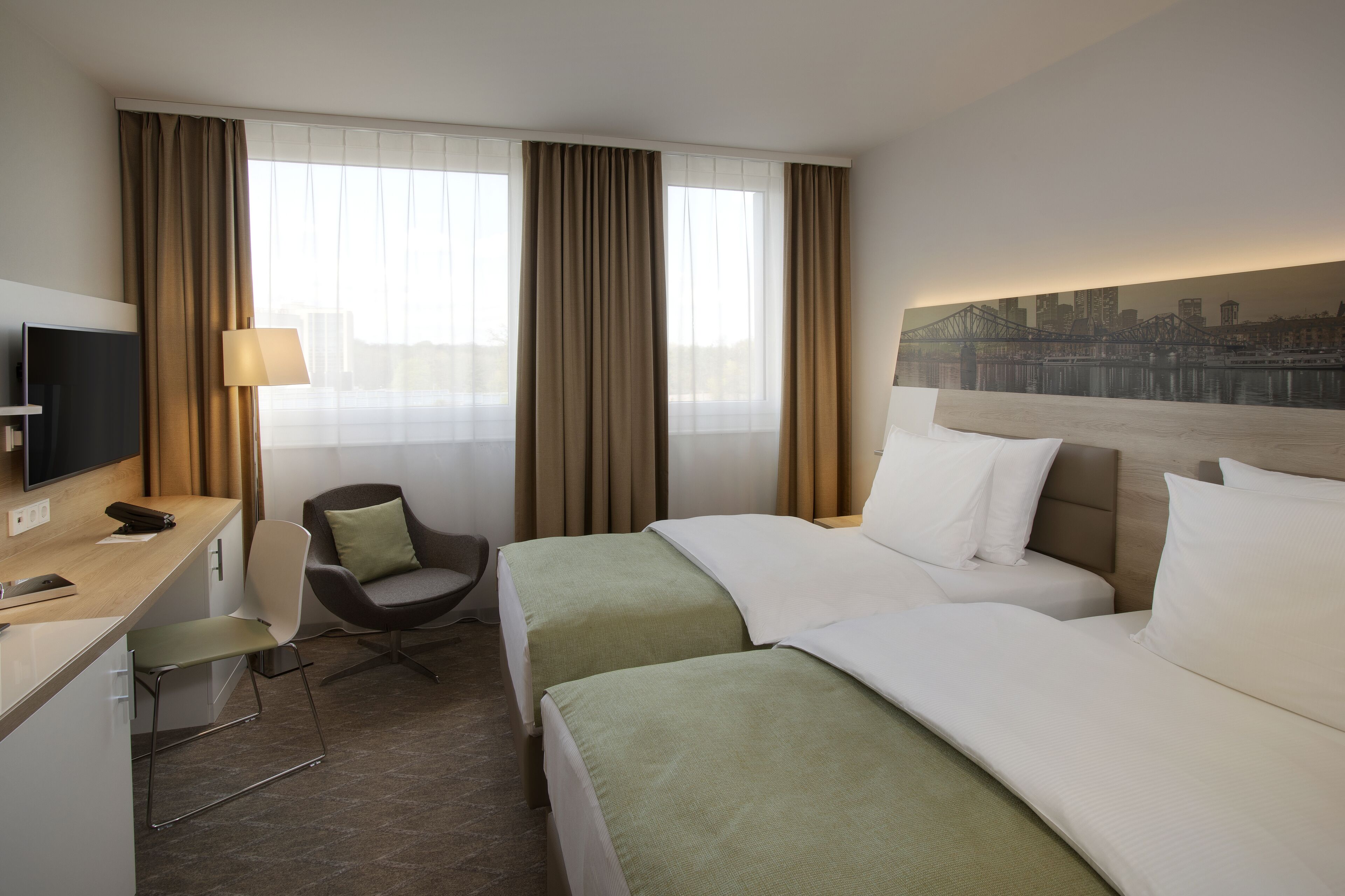 Quarto de hotel com duas camas, uma mesa com televisão, uma cadeira e um mural com vista para a cidade.