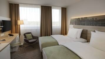 A hotel room with two beds, a desk with a TV, a chair, and a cityscape mural on the wall.