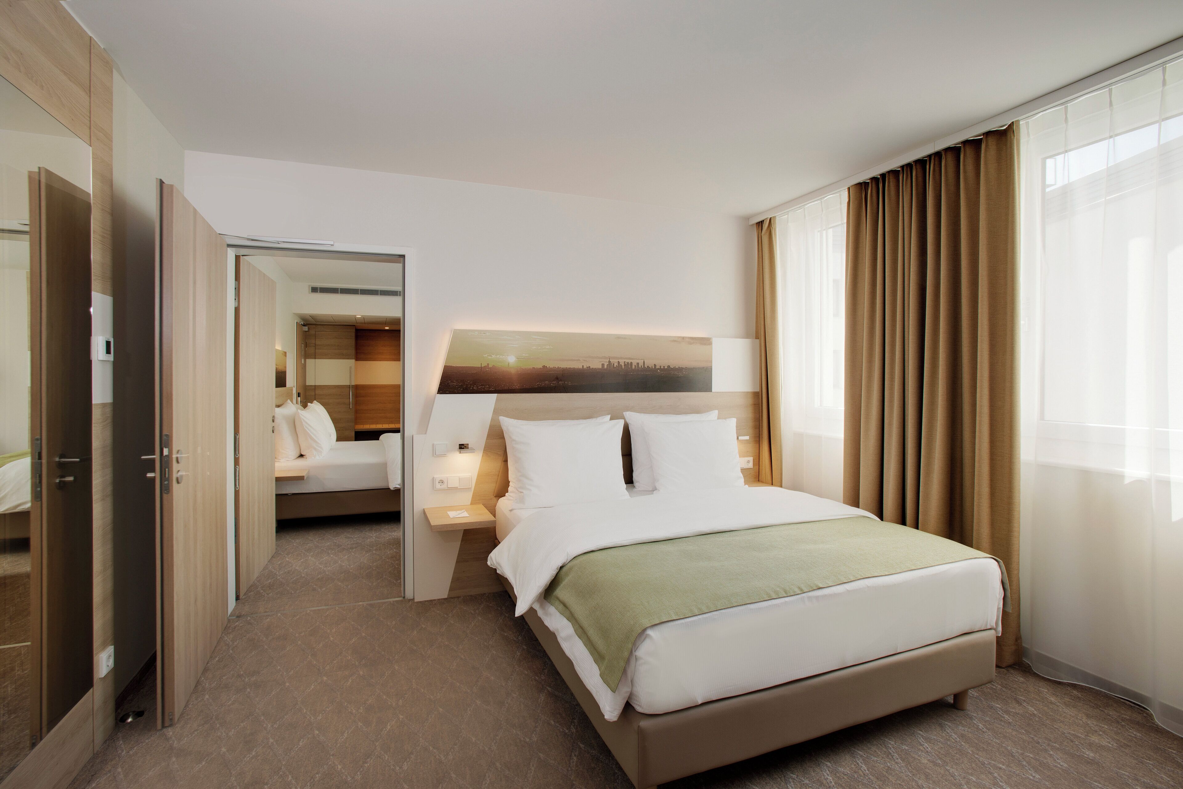 Habitación de hotel con cama, mesita de noche y vista a un paisaje urbano a través del ventanal.
