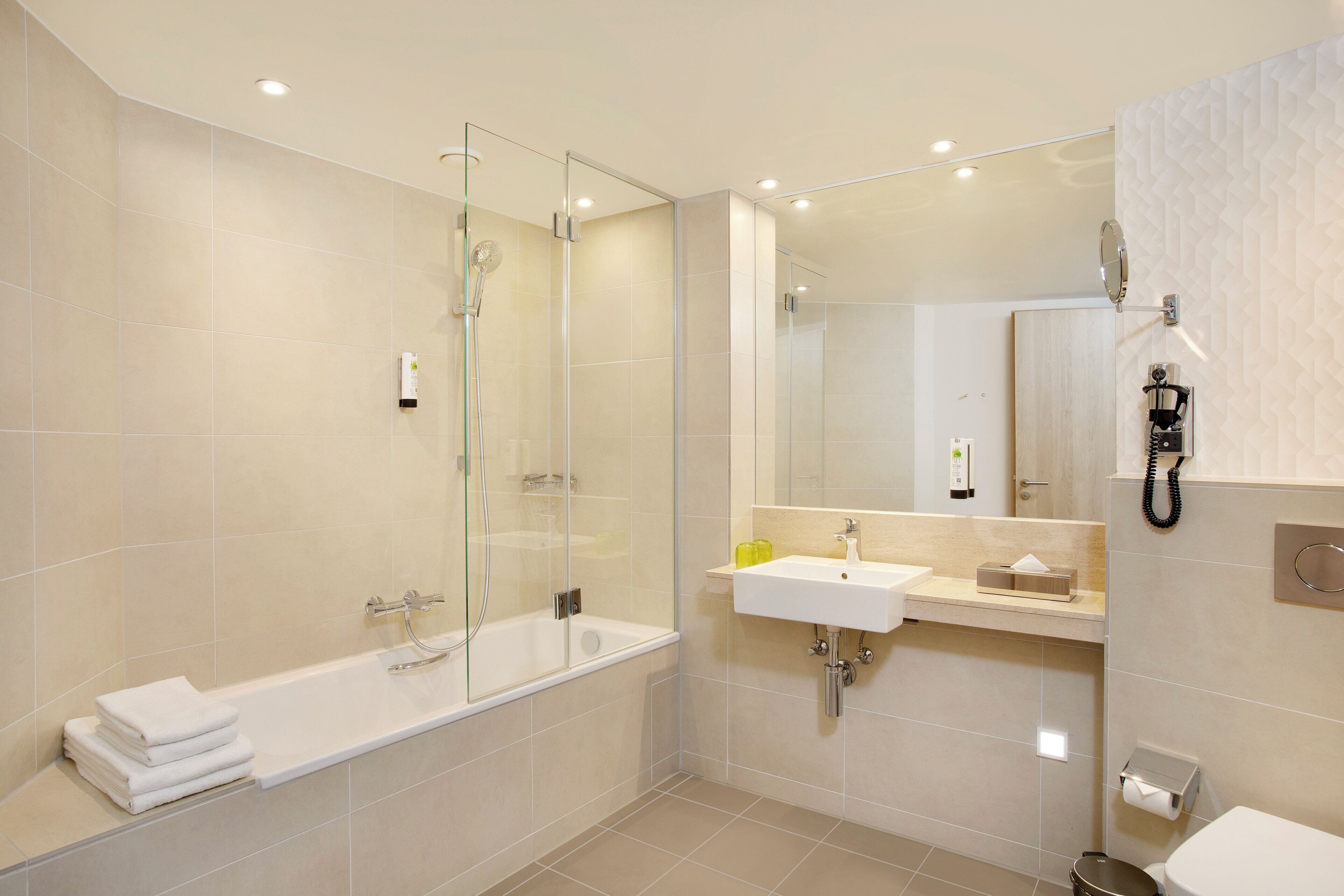 Ein modernes Badezimmer mit einer Glaskabine zur Dusche, einer weißen Badewanne, einem Waschbecken und einer Toilette.