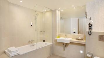 Ein modernes Badezimmer mit einer Glaskabine zur Dusche, einer weißen Badewanne, einem Waschbecken und einer Toilette.